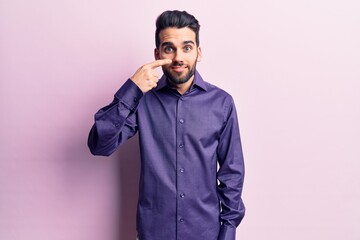 Young handsome man with beard wearing casual shirt pointing with hand finger to face and nose, smiling cheerful. beauty concept