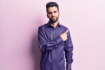 Young handsome man with beard wearing casual shirt pointing with hand finger to the side showing advertisement, serious and calm face