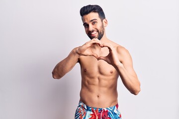 Young handsome man with beard shirtless wearing swimwear smiling in love doing heart symbol shape with hands. romantic concept.
