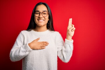 Young beautiful asian woman wearing casual sweater and glasses over red background smiling swearing...