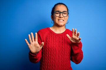 Young beautiful asian woman wearing casual sweater and glasses over blue background disgusted...