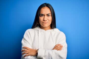 Young beautiful asian sportswoman wearing sweatshirt standing over isolated blue background skeptic...
