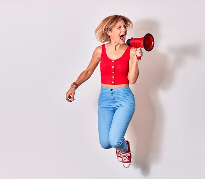 Young beautiful caucasian woman screaming using megaphone. Jumping over isolated white background