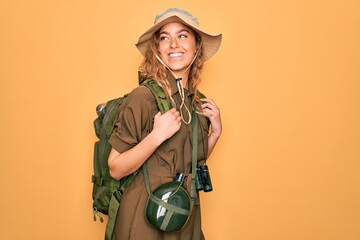 Young blonde explorer woman with blue eyes hiking wearing backpack and water canteen looking away...