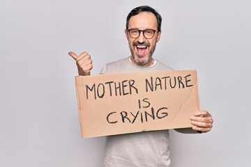 Middle age man asking for environment holding banner with mother nature is crying message pointing thumb up to the side smiling happy with open mouth