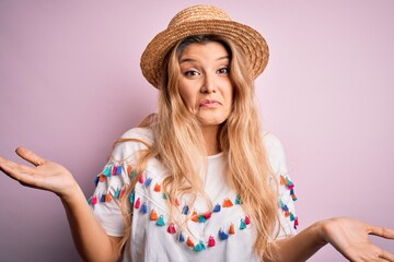 Young beautiful blonde woman wearing t-shirt and hat over isolated pink background clueless and...