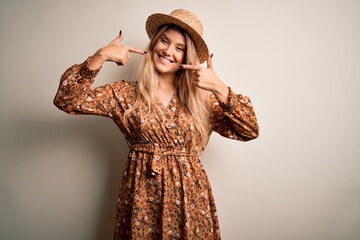 Young beautiful blonde woman wearing summer dress and hat over isolated white background smiling...