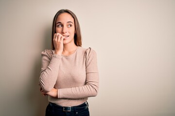 Young beautiful woman wearing casual sweater standing over isolated white background looking stressed and nervous with hands on mouth biting nails. Anxiety problem.