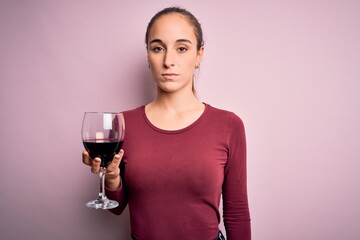Young beautiful woman drinking glass with red wine over isolated pink background with a confident expression on smart face thinking serious