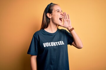 Young beautiful woman wearing volunteer t-shirt doing volunteering over yellow background shouting...