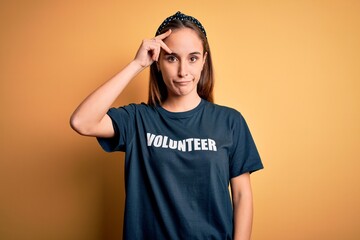 Young beautiful woman wearing volunteer t-shirt doing volunteering over yellow background worried...