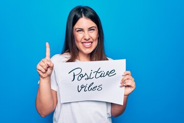 Young beautiful woman asking for optimist attitude holding paper with positive vibes message smiling with an idea or question pointing finger with happy face, number one