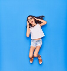Adorable hispanic child girl wearing casual clothes and glasses surprised with open mouth. Jumping...