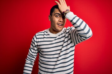Young brazilian man wearing casual striped t-shirt standing over isolated red background surprised...