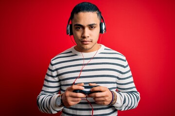 Young brazilian gamer man playing video game using joystick and headphones with a confident expression on smart face thinking serious