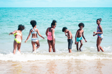 Group of six boys and girls standing in a line in shallow sea water, cute kids having fun on sandy summer beach, happy childhood friend playing on tropical sea