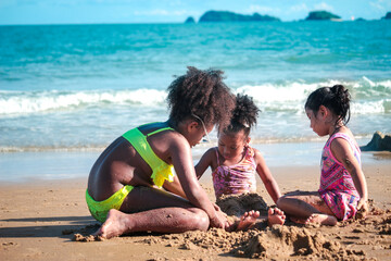 Cute kids having fun on sandy summer beach with blue sea, happy childhood friend making sand castle, playing with sandat on tropical beach