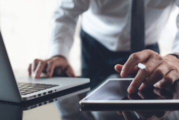 Closeup of businessman working on digital tablet and laptop computer in modern office