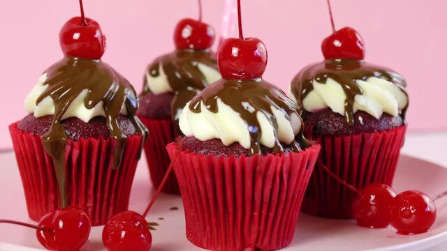 Red velvet cupcakes with chocolate sauce and cherries for dessert, parties and holiday celebrations. Closeup dolly shot.