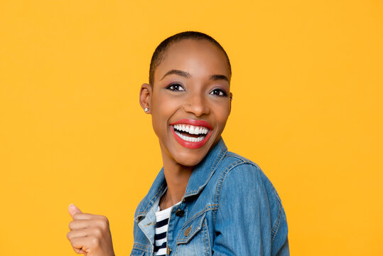 Close up portrait of cheerful excited smiling young African American woman with clenching fist in isolated studio yellow background
