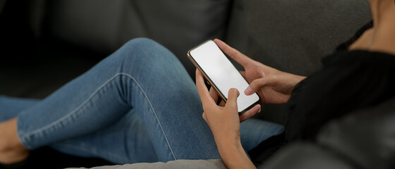 Female using mock-up smartphone while lying on the black couch in living room