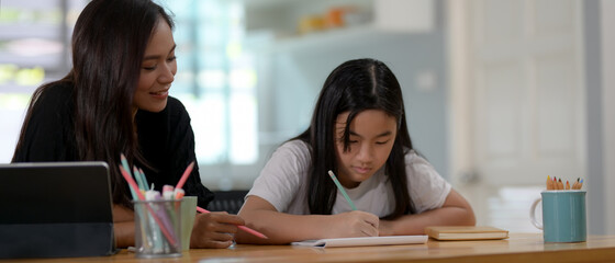 Private tutor and student homeschooling on wooden table with stationery in living room