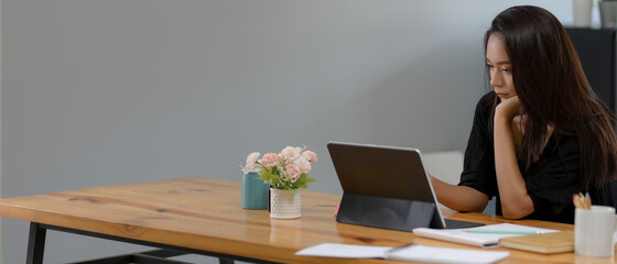 Young female employee working from home with digital tablet and paperwork on wooden desk