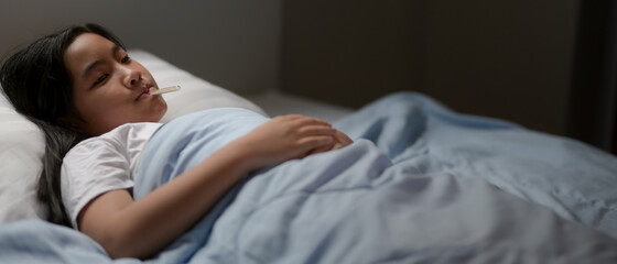 Sick girl lying on the bed while  take the temperature with thermometer in her mouth