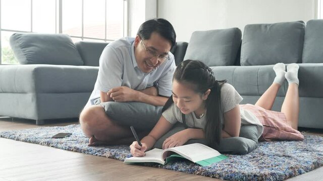 Cute little girl and her handsome father are using a digital tablet and smiling while lying on the floor at home
