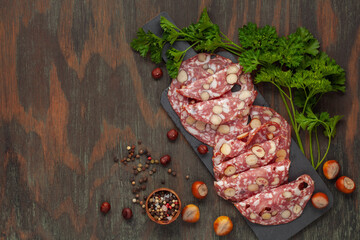 Smoked sausage salami with hazelnuts in a wooden plate on the table. Top view