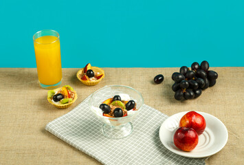 tartlet with fruit with whipped cream, a glass of juice and fruits on the table on a blue background.