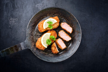 Traditionelles frittiertes Steak vom Kalb mit Zitronenscheibe und Kräuter als Draufsicht in einer rustikalen alten schmiedeeisernen Pfanne mit Textfreiraum
