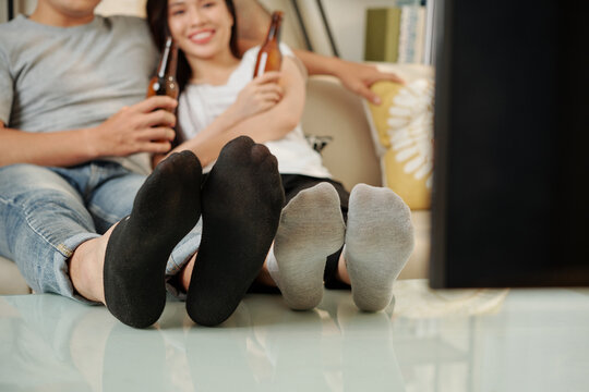 Boyfriend and girlfriend putting feet on coffee table when drinking beer and watching tv at home