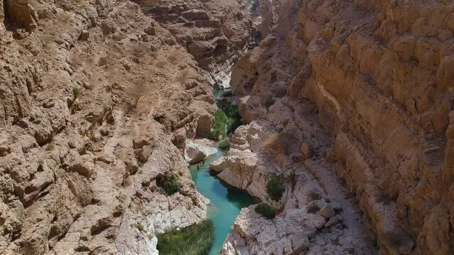 Aerial view panning down overlooking amazing oasis between huge mountains and rocks called Wadi Bani Khalid in Oman.