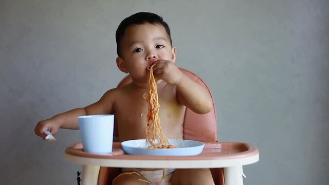 Asian boy eatting on high baby chair.