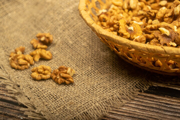 Peeled walnuts in a wicker basket and peeled walnuts scattered on a wooden table covered with rough-textured burlap. Healthy diet. Fitness diet. Close up.