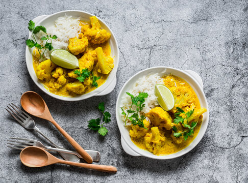 Indian food - vegetarian cauliflower curry with rice, cilantro, lime on grey background, top view