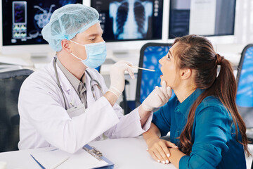 Physician in medical bouffant cap and mask using spatula when checking throat of patient
