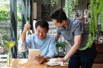 Portrait of a young man teaching his father how to use laptop computer. Son helping Dad to use the laptop. Father and Son using a laptop together at cafe.