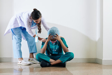 Nurse reassuring stressed tired female surgeon working over hours due to coronavirus pandemic