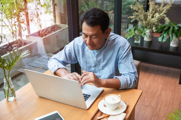 Old man using laptop computer working in cafe with relaxing.