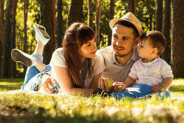 Family vacation. Father. mother and son on the picnic in the park. Young family are lying on the grass.