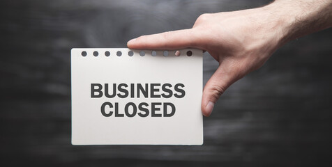 Male hand showing Business Closed text in paper.