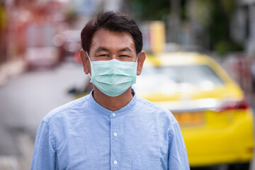 Old man wearing mask protective for spreading of disease virus Covid-19 and air smog pollution with PM 2.5 on street in  Bangkok city, Thailand.
