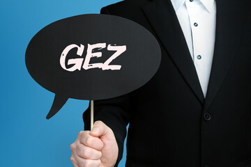 GEZ (Gebühreneinzugszentrale). Mann im Anzug hält Sprechblase in der Hand. Der Text GEZ steht im...
