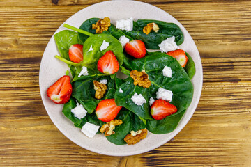 Fresh healthy salad with strawberry, spinach, walnuts and feta cheese on wooden table. Top view