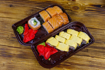 Set of sushi rolls in plastic boxes on wooden table. Top view. Sushi for take away or delivery of sushi in plastic containers