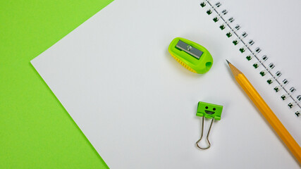 School Notepad with Yellow Pencil, Smile Binder Clip and Pencil Sharpener on Green Background. Spiral notebook on table. Business, office supplies or education concept