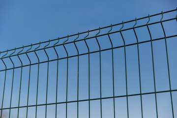 Steel grill fence with wire against the blue sky
