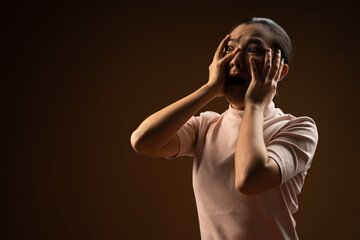 Asian woman scared screaming covering face by her hands standing isolated on beige background.